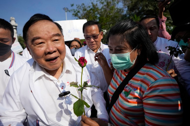 Prawit Wongsuwan greeting supporters. He's wearing a white shirt and looks happy. He's being given a red rose 