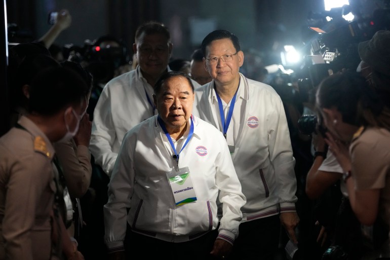 Thai Deputy Prime Minister and Prime Ministerial Candidate of the Palang Pracharath Party, Prawit Wongsuwan.  He wears a white shirt with the party logo and is followed by party officials.  He has a cord around his neck.