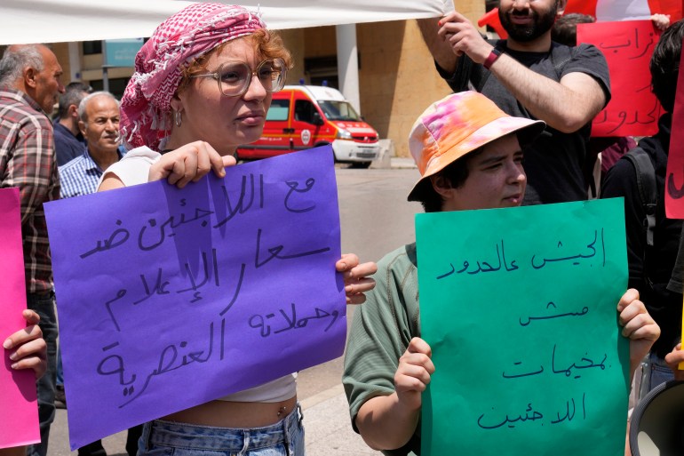 Pengunjuk rasa memegang spanduk bertuliskan "Dengan para pengungsi melawan kegilaan media dan kampanye rasis" Dan "Tempat tentara itu di perbatasan, bukan di pengungsian" dalam bahasa Arab selama pawai Hari Buruh yang diadakan oleh kelompok kiri di Beirut, Lebanon, Senin, 1 Mei 2023.