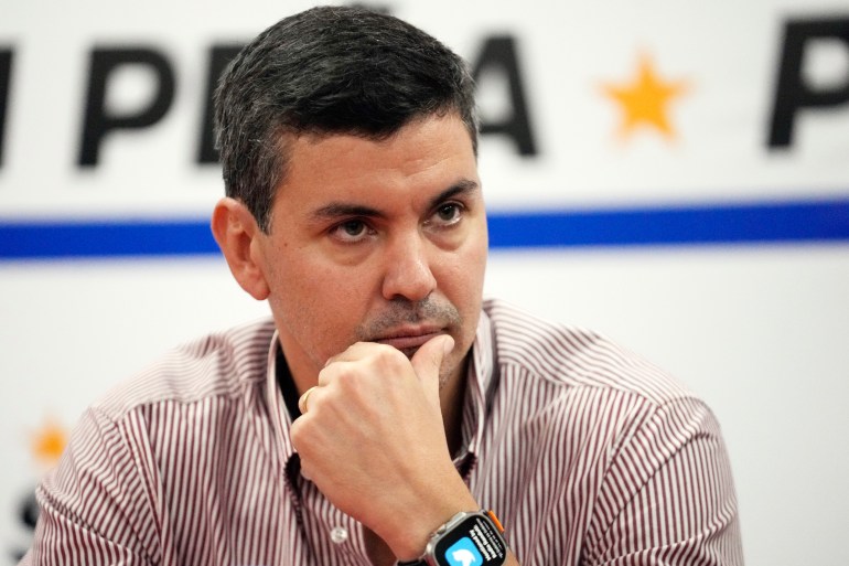 Santiago Peña sits at a press conference with one hand on his chin