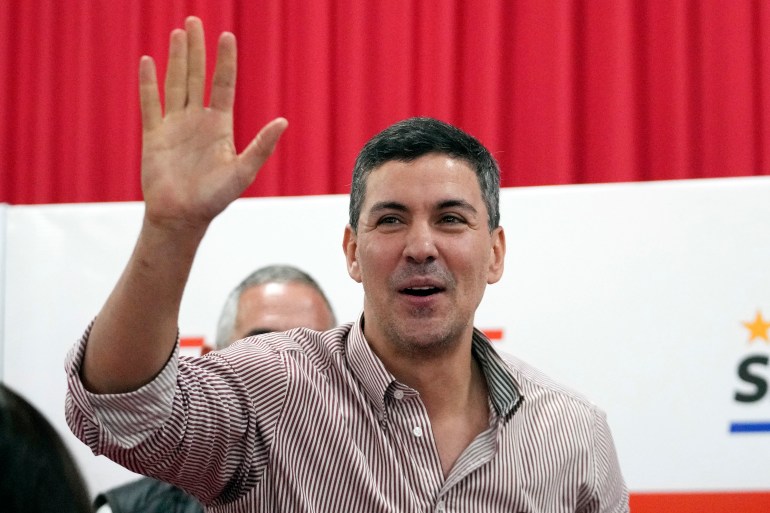 Santiago Pena waves against a red and white backdrop