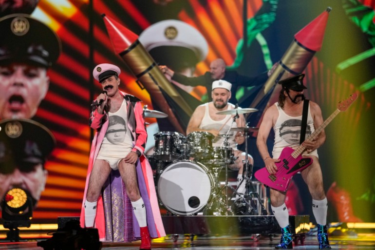 Deje 3 croatas en el escenario, vestidos con pantalones cortos y solteros.  El baterista está en el medio. 
