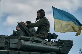 A Ukrainian tank near Bakhmut. There is a soldier on top and a Ukrainian flag flying behind.