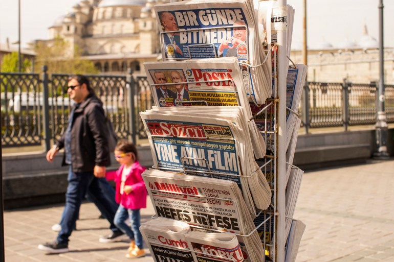 People walk past a rack with Turkish newspapers 
