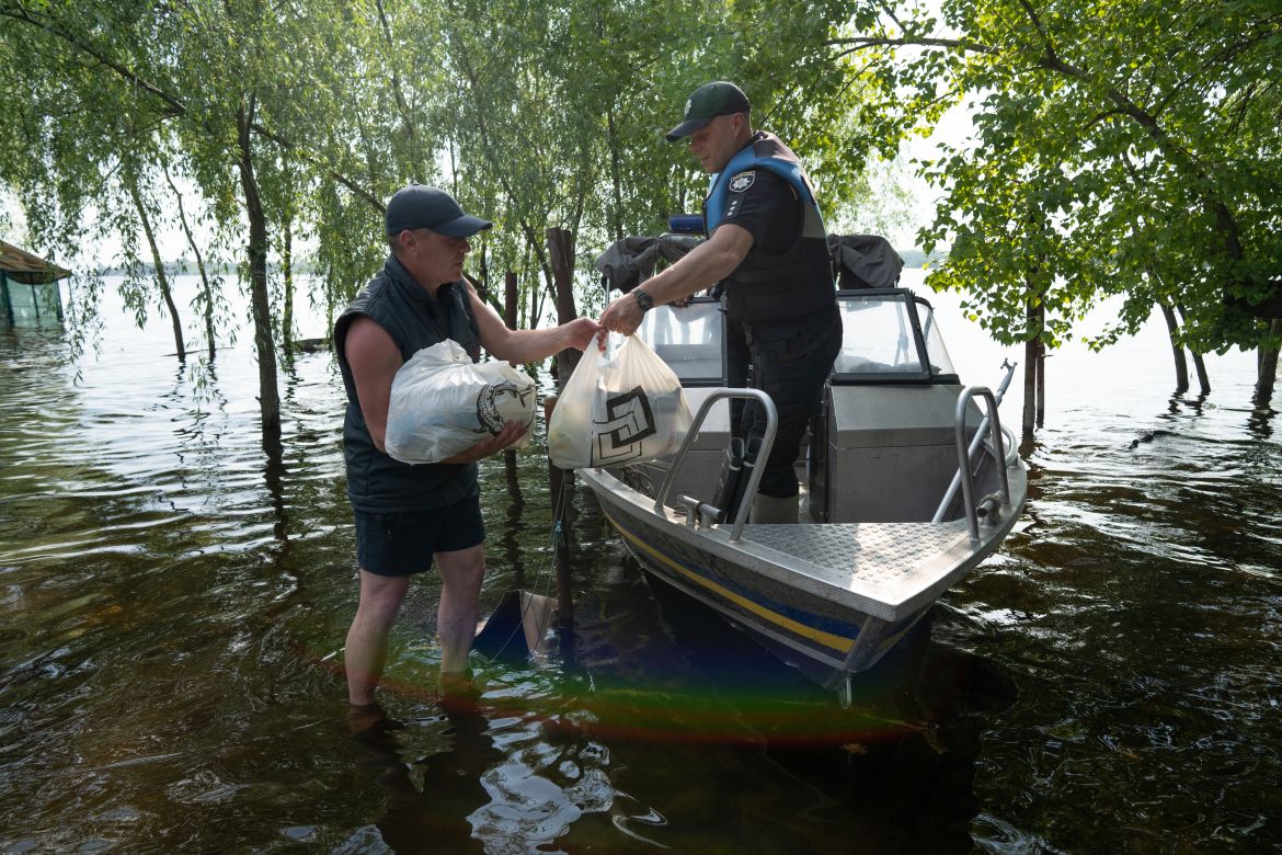 A local man receives humanitarian aid from a police officer during patrol area of Kakhovka reservoir