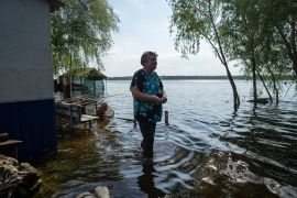 Lyudmila Kulachok, 54, stands in the flooded courtyard of her house on an island at Kakhovka Reservoir on Dnipro River [Evgeniy Maloletka/AP Photo]