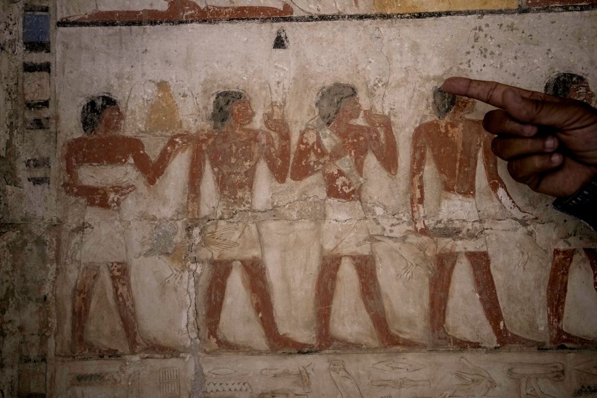 An Egyptian archeologist points at a colored painting showing offering sacrifices at a recently uncovered tomb