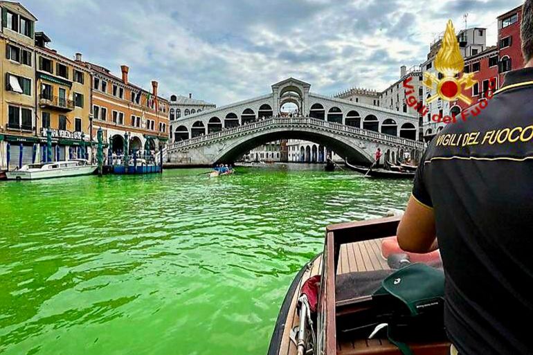 In this image released by the Italian firefighters, a firefighter on a boat looks at the arched Rialto Bridge along Venice's historical Grand Canal as a patch of phosphorescent green liquid spreads in it