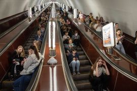 People sitting on escalators in the Kyiv metro as they take shelter from Russian air raids.