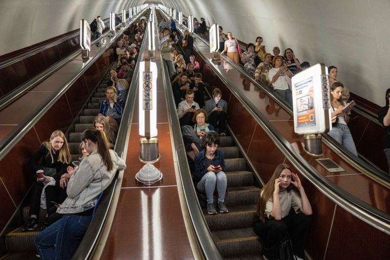 People sitting on escalators in the Kyiv metro as they take shelter from Russian air raids.