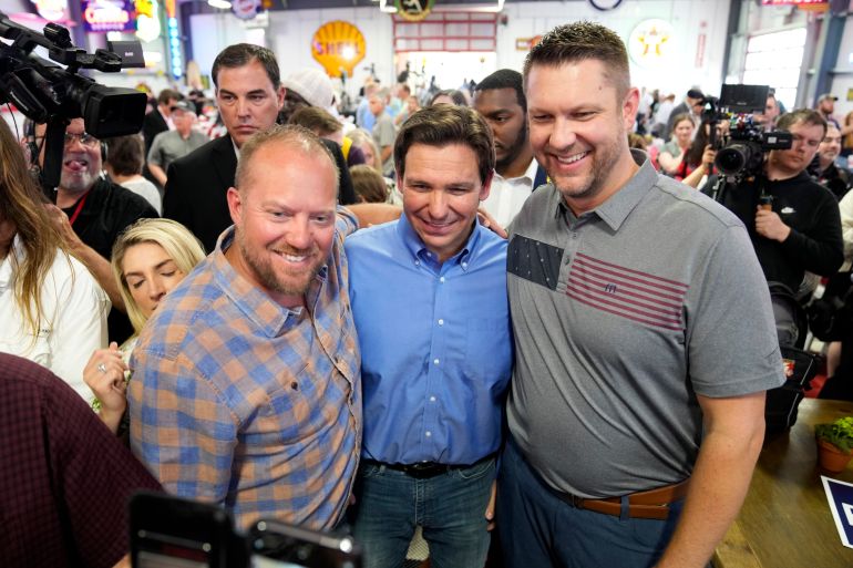 Governor Ron DeSantis poses for a photo with two men at a busy hall in Sioux City, Iowa.