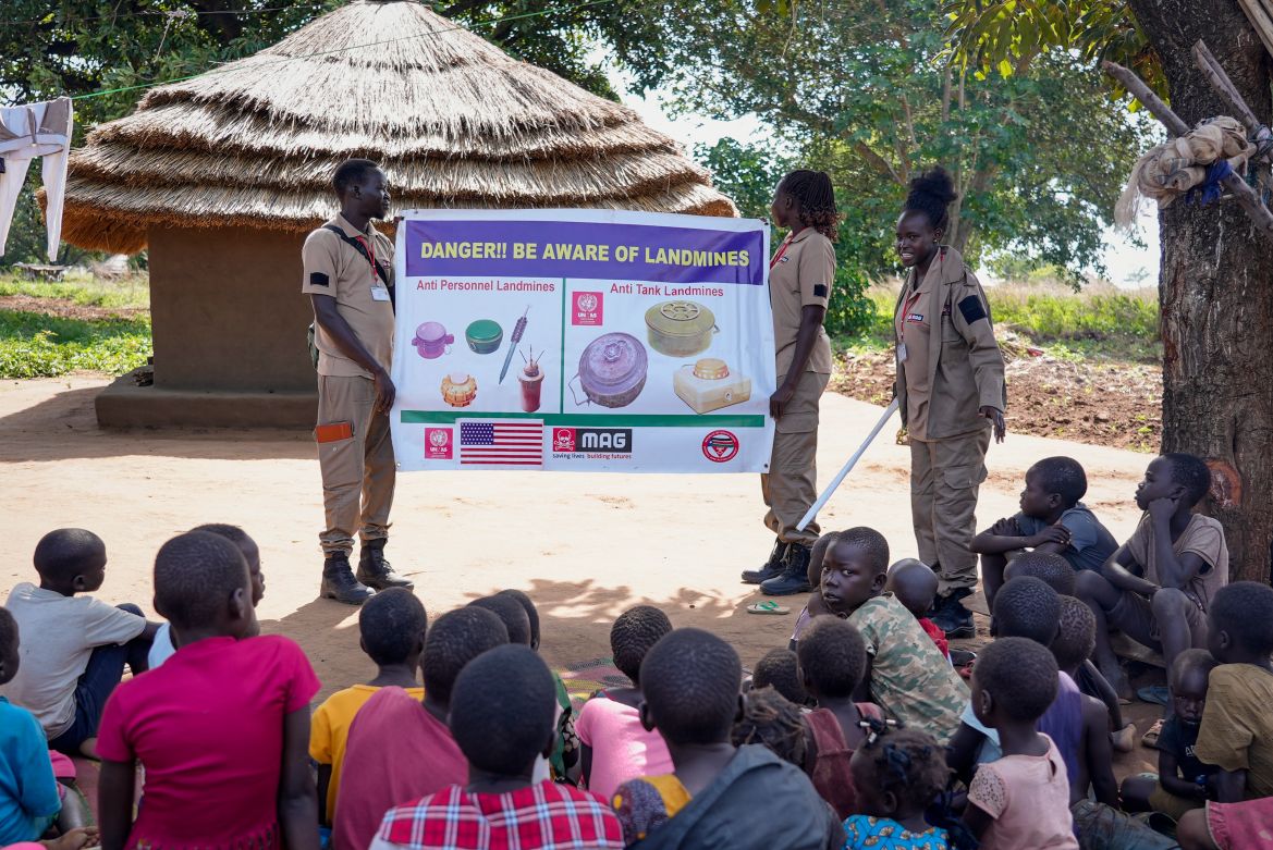 Staff from the Mines Advisory Group (MAG) teach children about the risks of unexploded mines, in Moli village