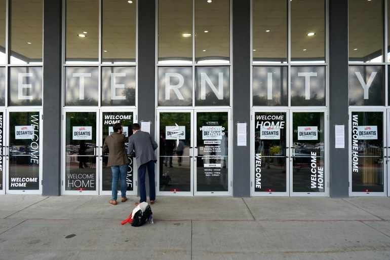 Glass doors, with the word "eternity" written above them, are decorated with DeSantis signs by two men.