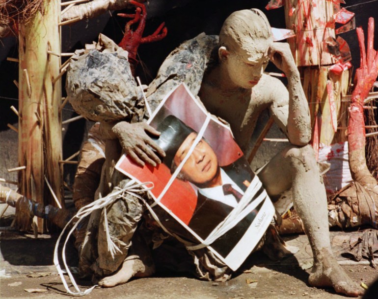 Cubierto de barro, un estudiante muestra su interpretación de la caída en desgracia del ex presidente Soeharto durante una actuación en el Centro de Artes Taman Ismail Marzuki en Yakarta el miércoles 3 de junio de 1998. El estudiante sostiene un póster del retrato de Soeharto.  (Muchtar Zakaria/AP)