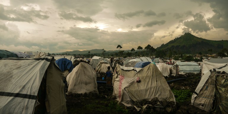 Tenda berdiri di tepi genangan air hujan di kamp Bushagara, DRC.  (Sophie Neiman/Al Jazeera)