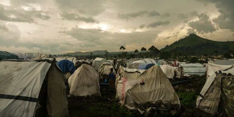 Tents perched on the edge of rain puddle in Bushagara Camp, DRC. [Sophie Neiman/Al Jazeera]
