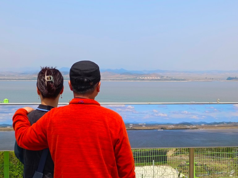 Couple looks at North Korea across the mouth of the Han River at the Ganghwa Peace Observatory.  It is a sunny day with a cloudless sky