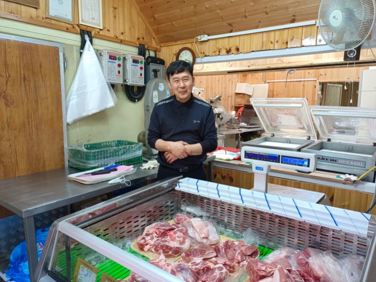 Choi Seong-ho tersenyum di sebelah kulkas dagingnya di Pasar Daeryong di perbatasan Korea Utara. 