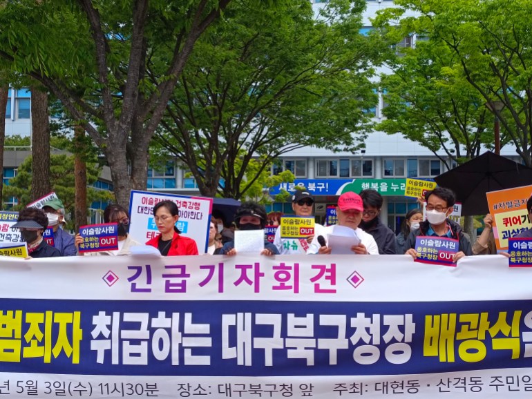 A small group of anti-mosque protesters gather outside the Buk district office. They are standing behind a big banner and some have smaller banners in Korean with the English word 'OUT!'