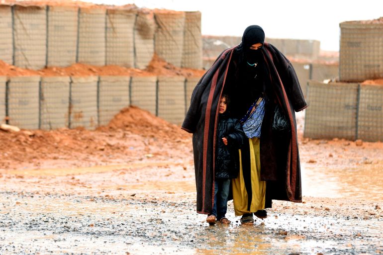 A Syrian refugee from the informal Rukban camp, which lies in no-man's-land off the border between Syria and Jordan in the remote northeast, walks in the rain, as she shelters a young child outside a UN-operated medical clinic immediately on the Jordanian-side on March 1, 2017.