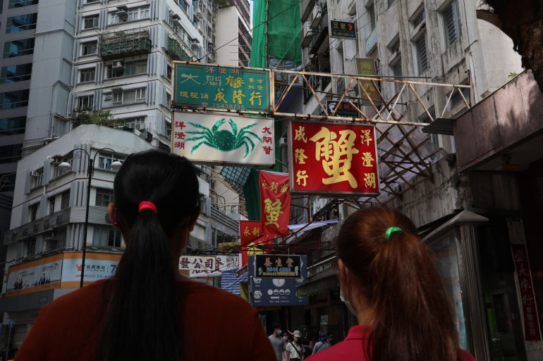 Two women who are domestic workers in Hong Kong. They are silhouetted against skyscrapers and the neon signs with their backs to the camera.