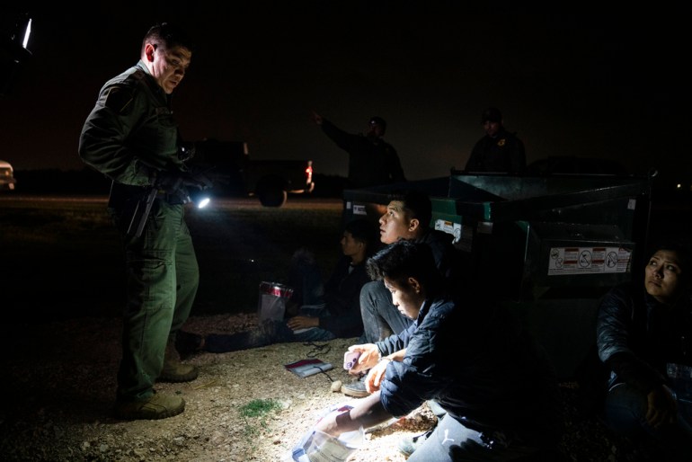 Migrants sit under the flashlight of a US Border Patrol agent