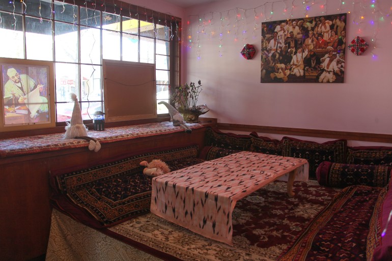 A low-slung table sits on an ornate carpet, beside a window and beneath a painting.