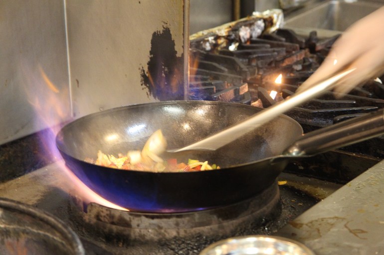 Flames cradle a black wok as someone stirs its contents.