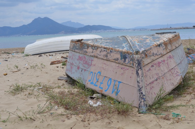 an upturned boat on the shore, water behind