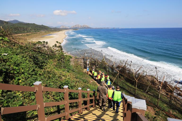 Hikers descend stairs to the sea.  They wear reflective shirts.  They walk to an empty beach with waves crashing on the shore