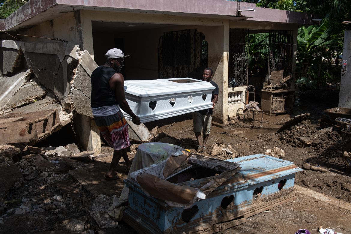 epa10676467 Two men carry a coffin next to a damaged house on a muddy street from heavy rains, in Leogane, Haiti,