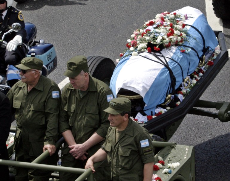 Pejabat militer dengan truk menyeret peti mati yang ditutupi dengan bendera Argentina melalui jalan-jalan.