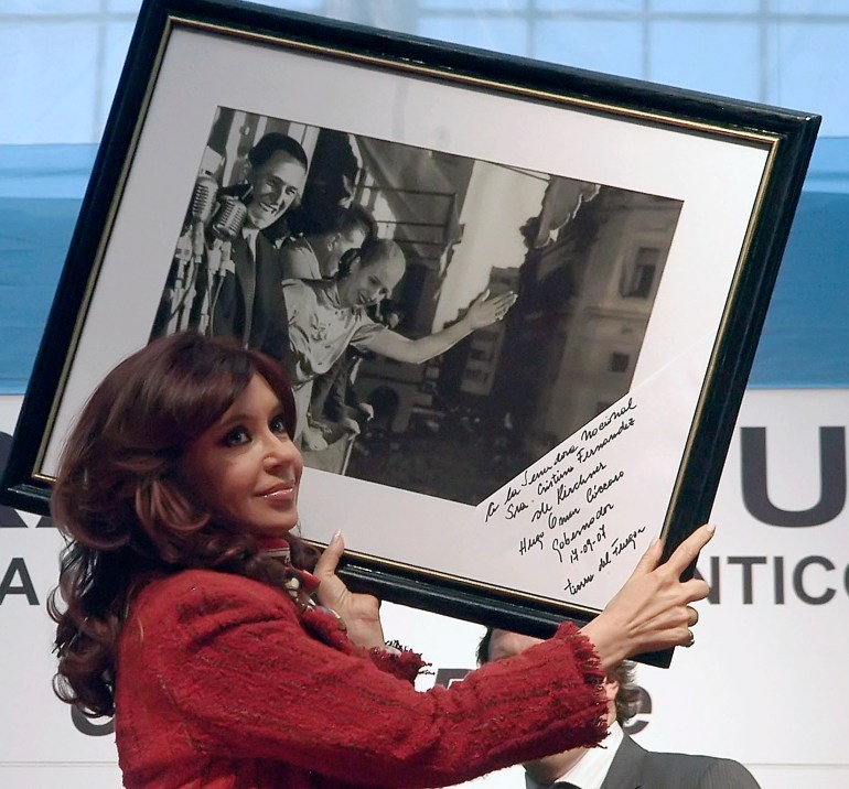 A woman in a red suit hoists a large framed photograph up on one shoulder