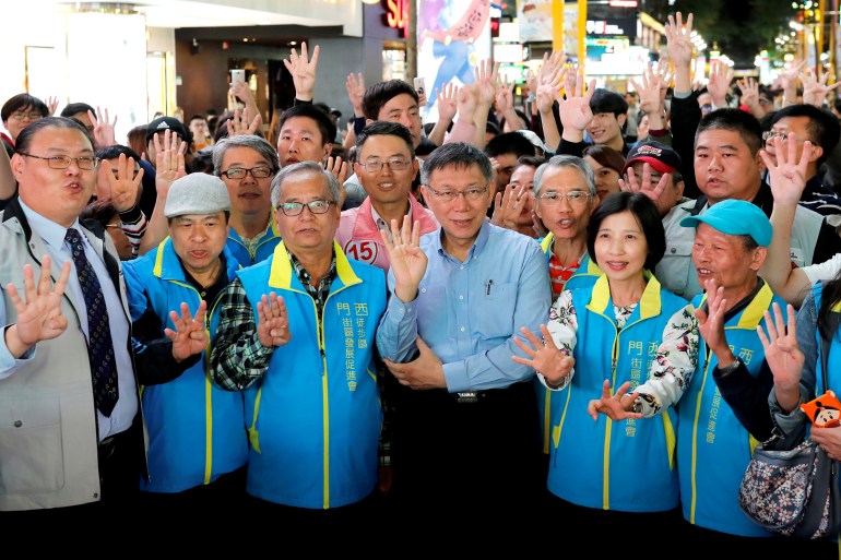 Ko Wen-je surrounded by supporters. He is wearing a blue shirt and holding up his hand to show four fingers (his candidate number). The supporters are doing the same.
