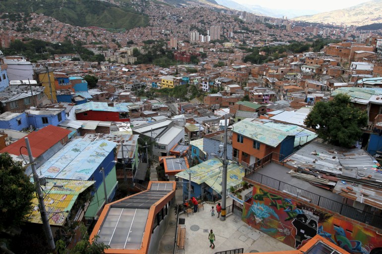 An aerial view of a neighborhood dominated by tin-roofed buildings, painted orange, red and blue, along a hill.