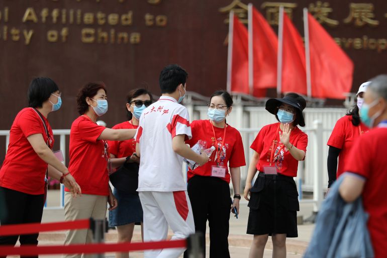 Kırmızı tişörtler giymiş öğretmenler, öğrencilerine Gao Kao'da iyi şanslar diler.  Bir okulun dışındalar.  Arkalarında kırmızı bayraklar var.