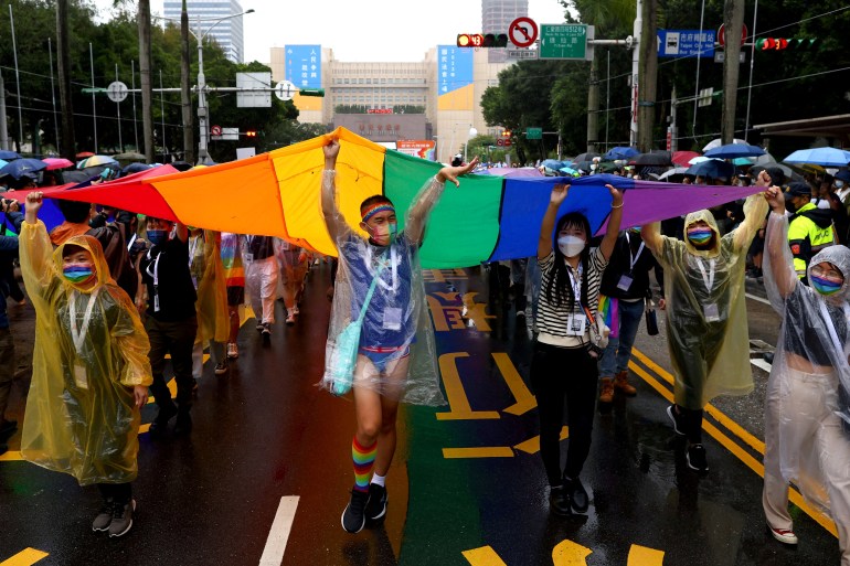People walking beneath a giant rainbow flag during pride in Taipei