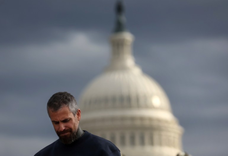 A man bows his head, while the US Capitol looks on in the background.