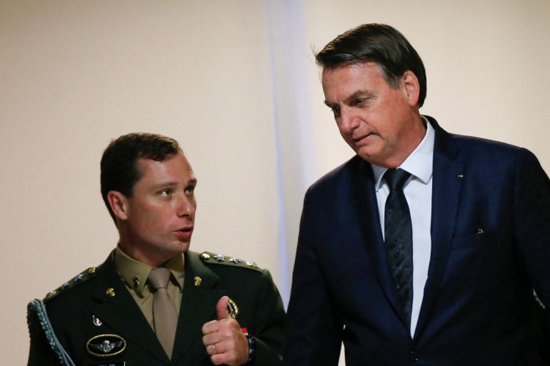 A man in a dark suit speaks with a man in military dress uniform, with stars along his shoulders.