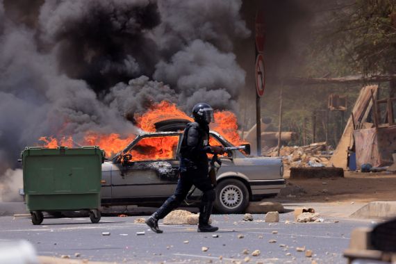 A riot police officer walks near a car set on fire during clashes between supporters of Senegalese opposition leader Ousmane Sonko and security forces after Sonko was sentenced to prison in Dakar