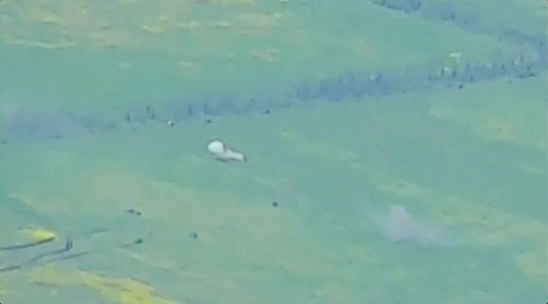 Rusia dice que las imágenes de drones muestran vehículos blindados moviéndose en un lugar desconocido.  El metraje es granulado y muestra una extensión de campos verdes con varios puntos negros y dos explosiones.  Hay una hilera de árboles detrás.