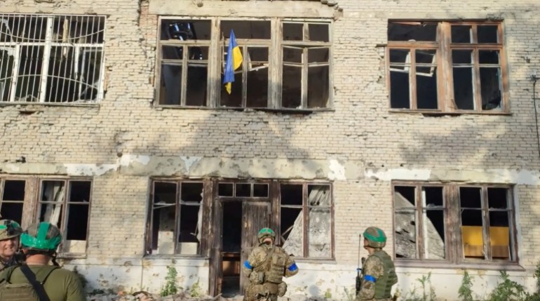 Ukrainian soldiers stand in front of a building with a Ukrainian flag during an operation that claims to liberate the first village in the counteroffensive, known as Blahodatne