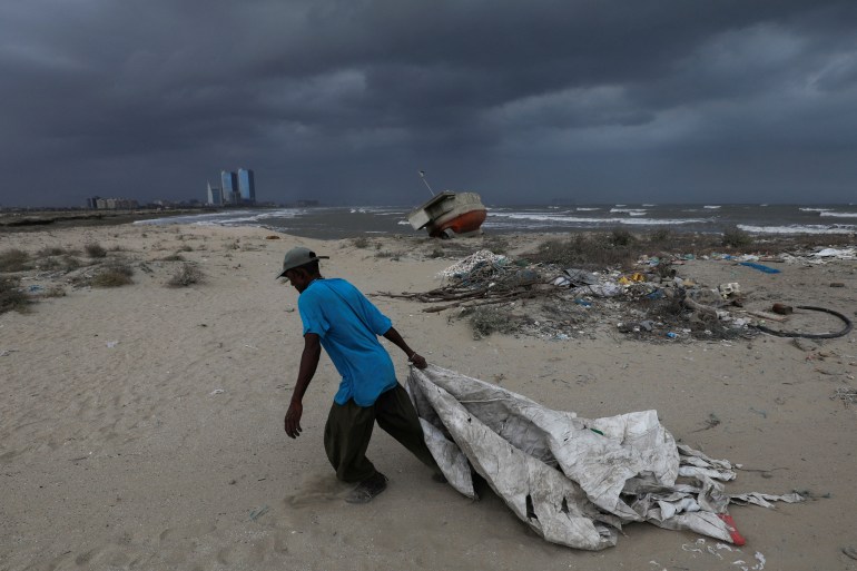 Sooraj, 32, a fisherman and diver, pulls a sheet to cover his belongings, with rain clouds in the background, before the arrival of cyclonic storm, Biparjoy, over the Arabian Sea, in Karachi, Pakistan June 15, 2023.