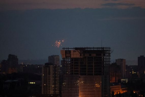 A photo of a drone exploding above Kyiv. The sky is almost dark with buildings silhouetted against it.