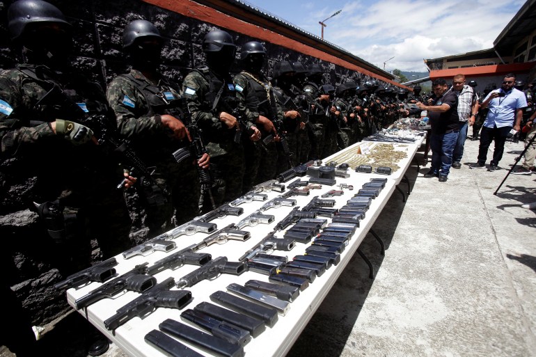 Guards stand behind a long white table, where guns and ammo are on display