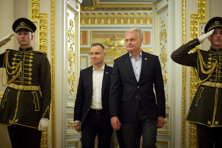 Polish President Andrzej Duda and Lithuanian President Gitanas Nauseda arrive for a joint press conference with Ukrainian President Volodymyr Zelenskyy.  The room is ornate and on either side of the door are two soldiers in ceremonial dress.