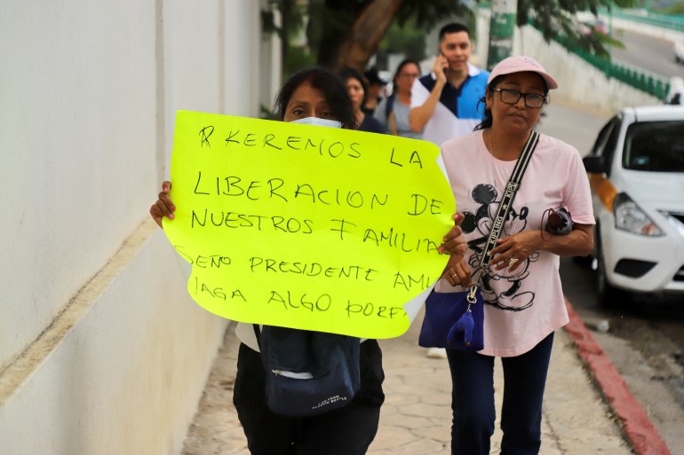 Seorang wanita memegang plakat kuning yang meminta pembebasan anggota keluarganya saat dia berjalan di jalan.