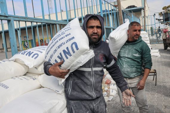 Palestinians carry bags of flour received as aid to poor families, at the United Nations Relief and Works Agency for Palestine Refugees (UNRWA) distribution center