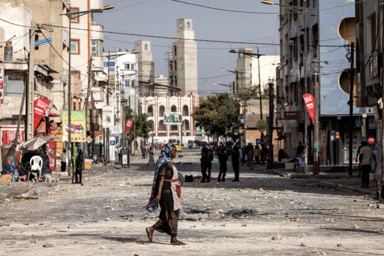 Stones and debris are seen in a street in Dakar as a woman crosses the street in the aftermath of a protest.