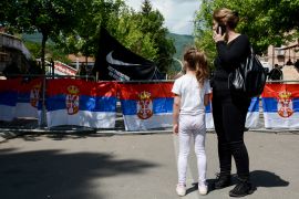 A woman with her child stands outside the Zvecan town hall in northern Kosovo as tensions remain high [Stringer/AFP]